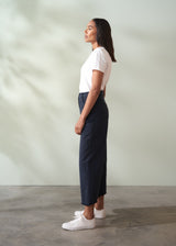 Woman wearing a white top and navy wide leg trousers standing against a plain background