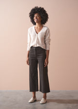 Woman wearing a light-colored cardigan and dark pants against a beige background