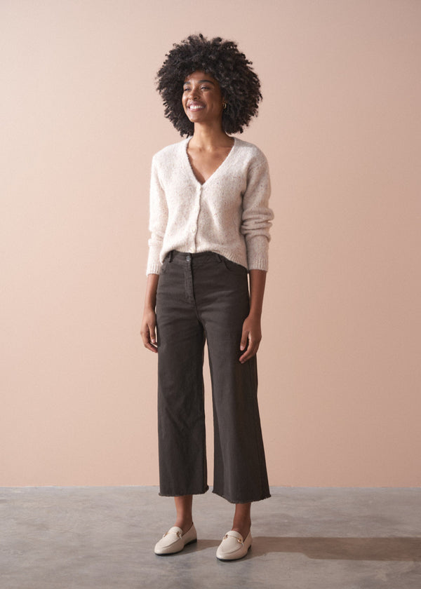 Woman wearing a light-colored cardigan and dark pants against a beige background