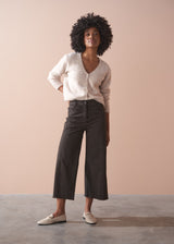 Person wearing dark brown wide-leg trousers and a beige cardigan against a plain background