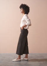 Person wearing dark brown wide-leg trousers and a beige cardigan against a plain background