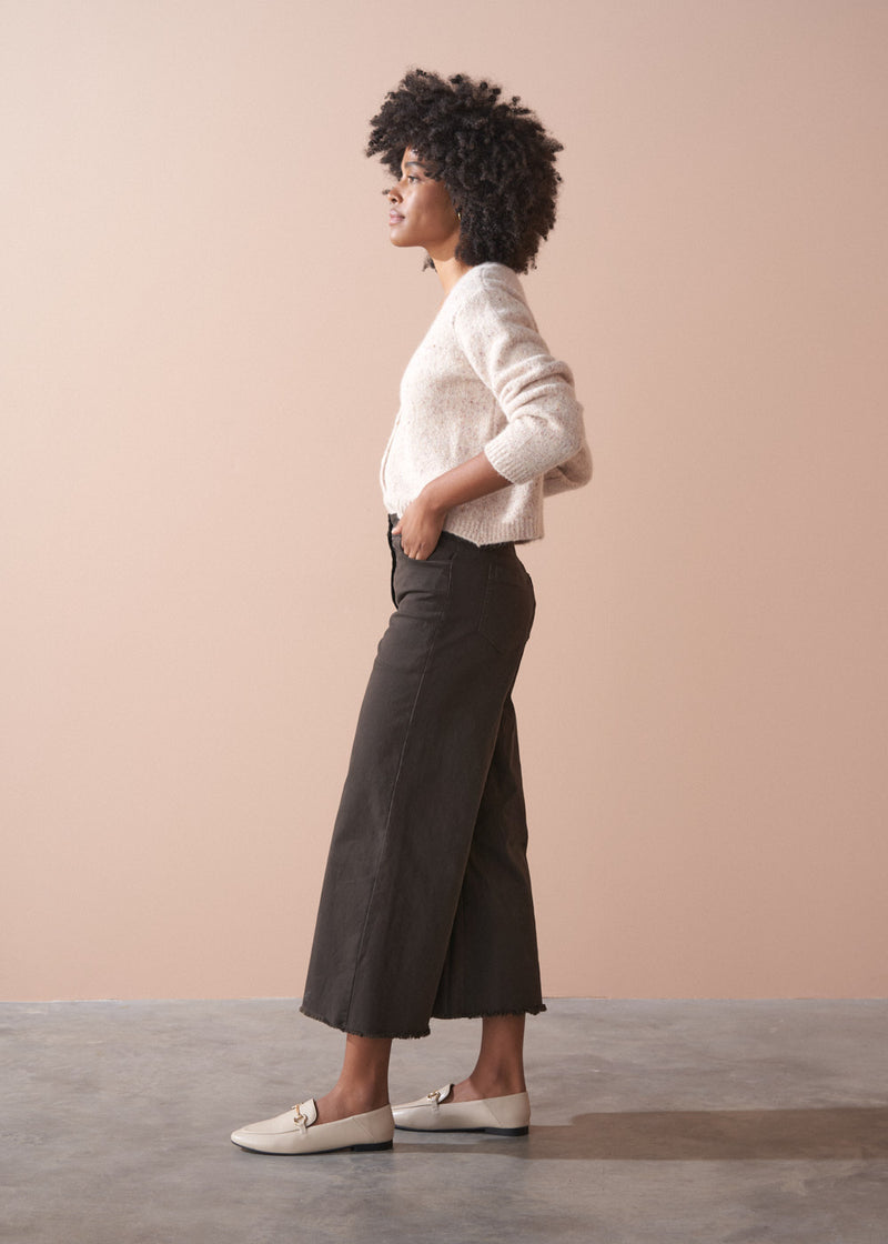 Person wearing dark brown wide-leg trousers and a beige cardigan against a plain background