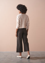 Person wearing dark brown wide-leg trousers and a beige cardigan against a plain background