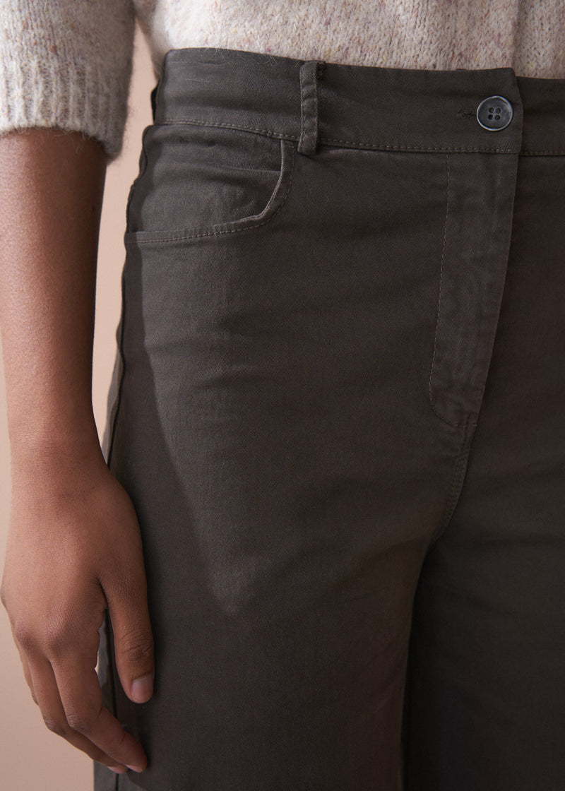 Person wearing dark brown wide-leg trousers and a beige cardigan against a plain background