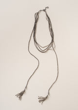 A multi-strand silver-toned beaded necklace with long fringe tassels at the ends, displayed flat against a light beige background.
