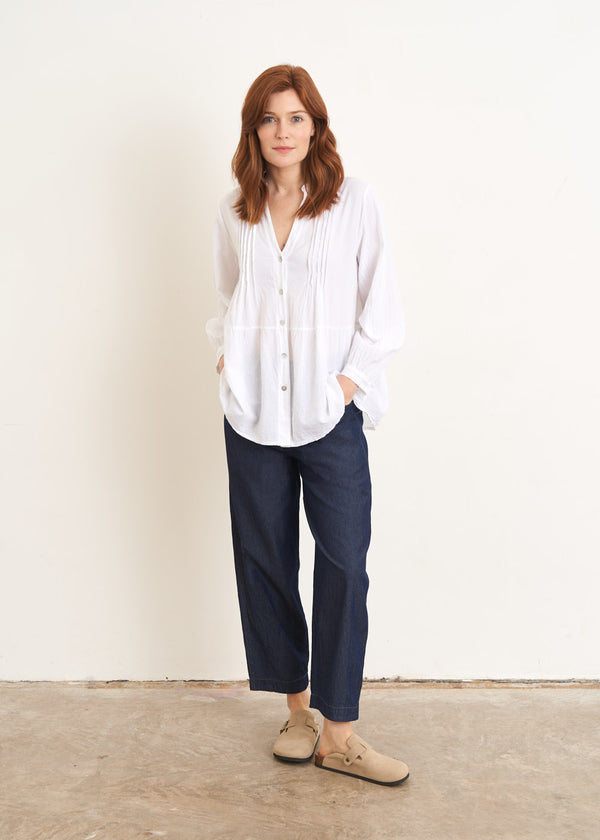 A model wearing a white long sleeved button down pin  tucked shirt with blue jeans