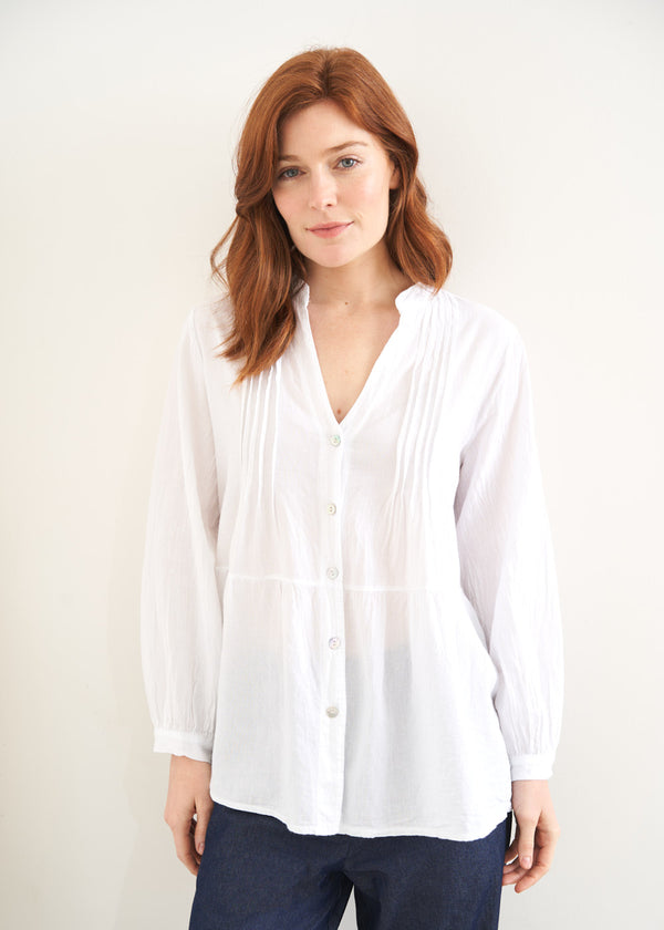 A model wearing a white long sleeved button down pin  tucked shirt with blue jeans