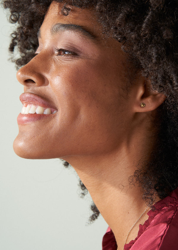 Woman wearing small gold hear stud earrings
