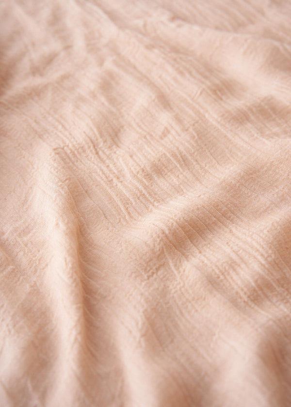 Light oatmeal scarf with frayed edges on a light gray background