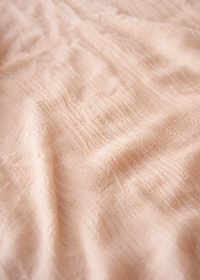 Light oatmeal scarf with frayed edges on a light gray background