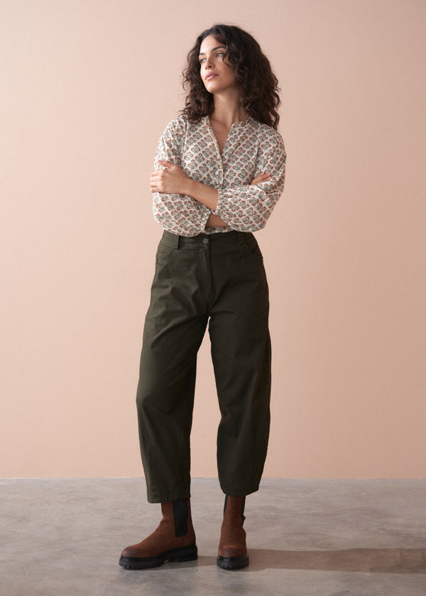 Woman wearing a patterned cotton blouse and green barrel leg trousers against a beige background