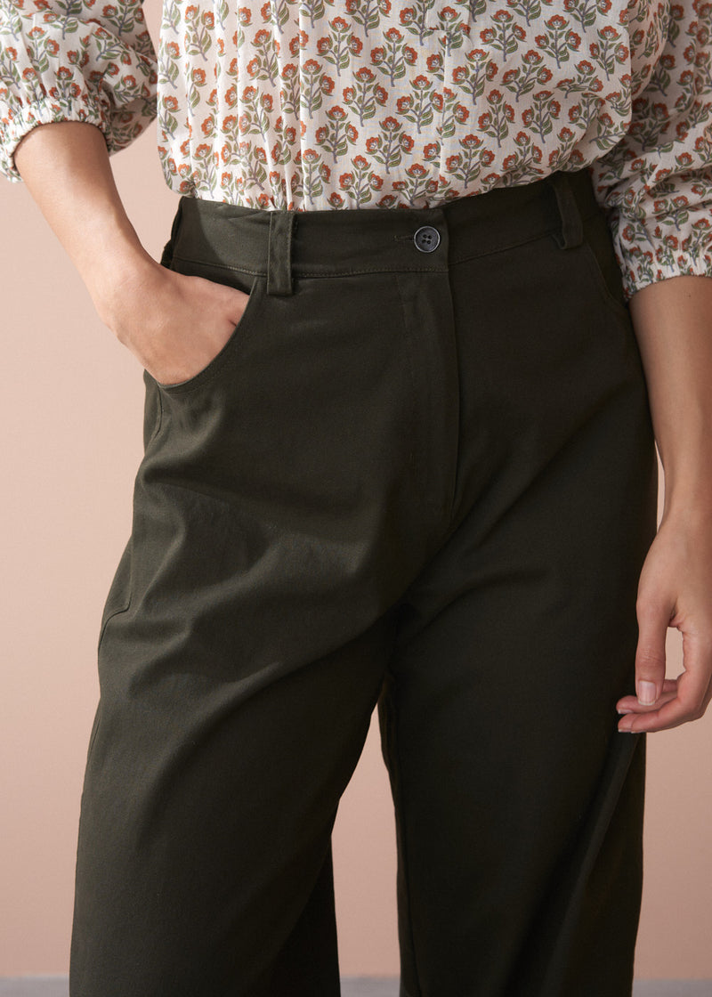 Woman wearing a patterned cotton blouse and green barrel leg trousers against a beige background
