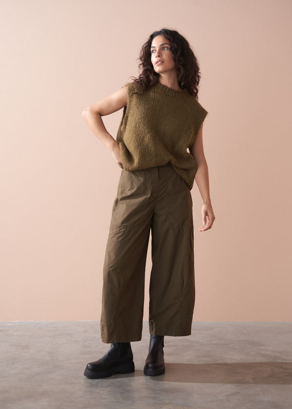 Woman wearing a green sleeveless top and wide-leg cargo trousers against a beige background