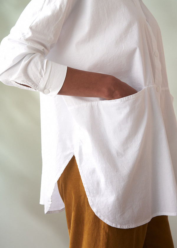 White shirt with rolled-up sleeves worn over a brown garment on a plain background