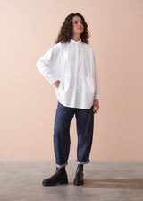 Woman wearing a white shirt and dark pants against a beige background