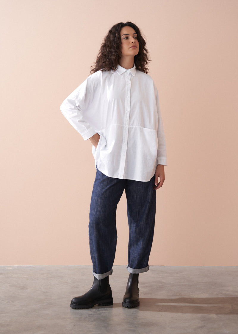 Woman wearing a white shirt and dark pants against a beige background