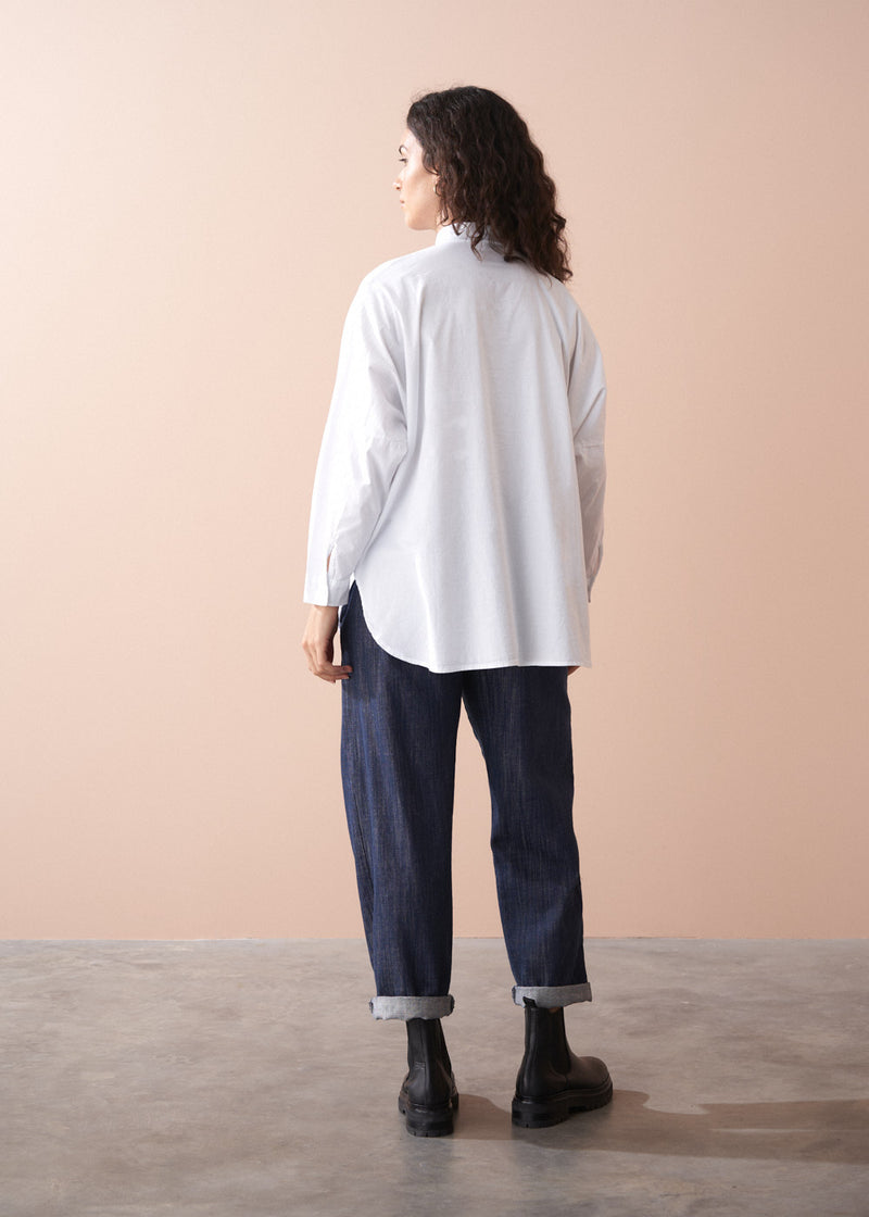 Woman wearing a white shirt, dark jeans, and black boots against a beige background