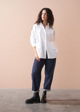 Woman wearing a white shirt and dark jeans against a beige background