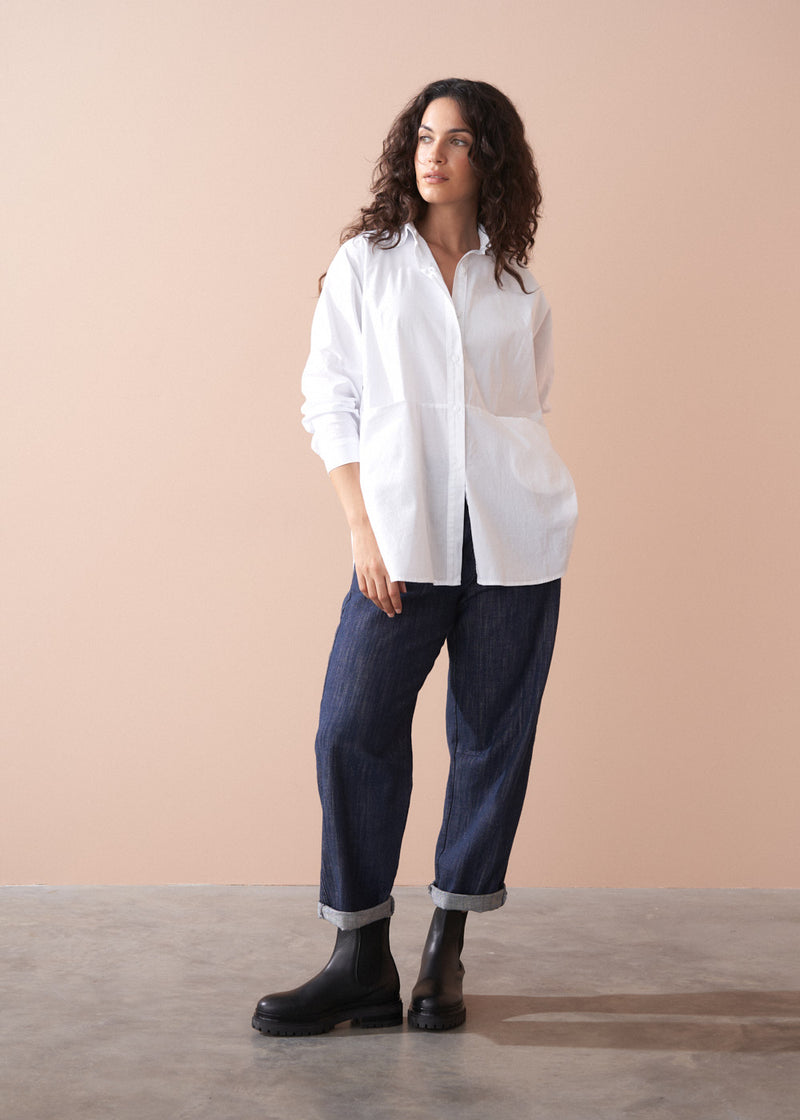 Woman wearing a white shirt and dark jeans against a beige background
