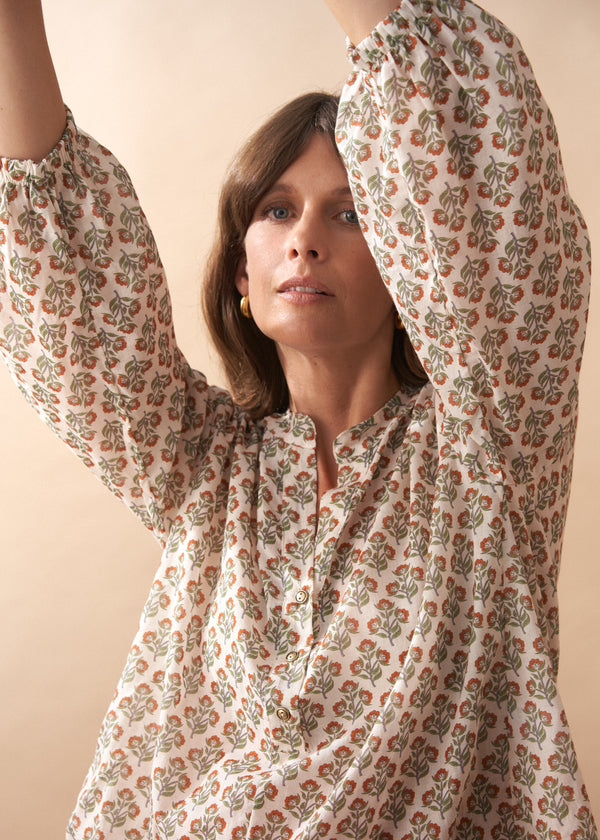 Woman wearing a floral patterned blouse with arms raised against a beige background