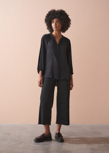 Woman wearing a black satin blouse and black wide leg trousers against a beige background