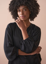 Woman wearing a black satin blouse and black wide leg trousers against a beige background