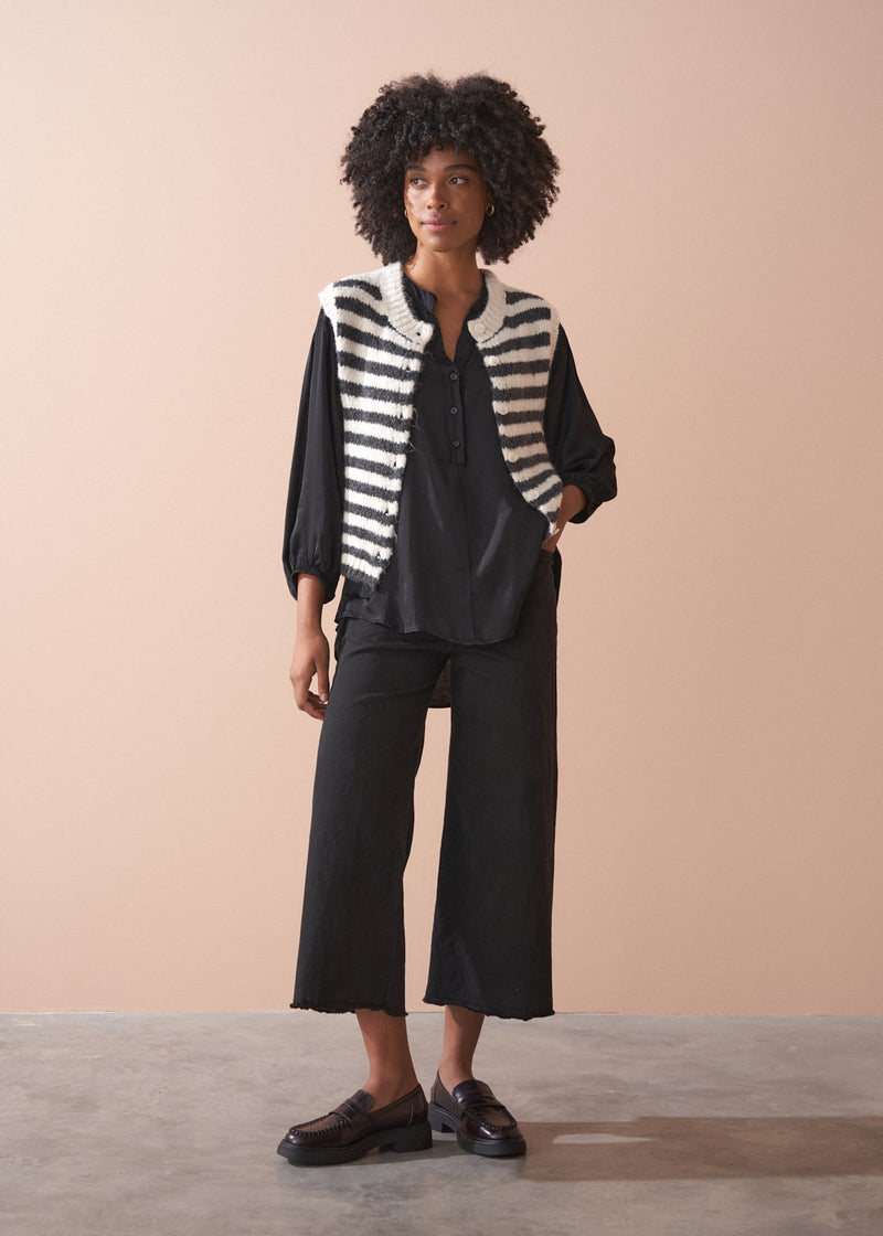 Woman wearing a black satin blouse and black wide leg trousers against a beige background