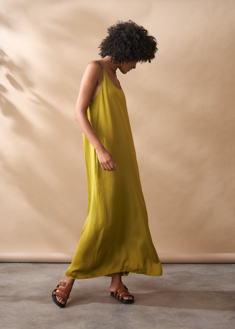 Woman wearing a yellow satin maxi dress against a beige background