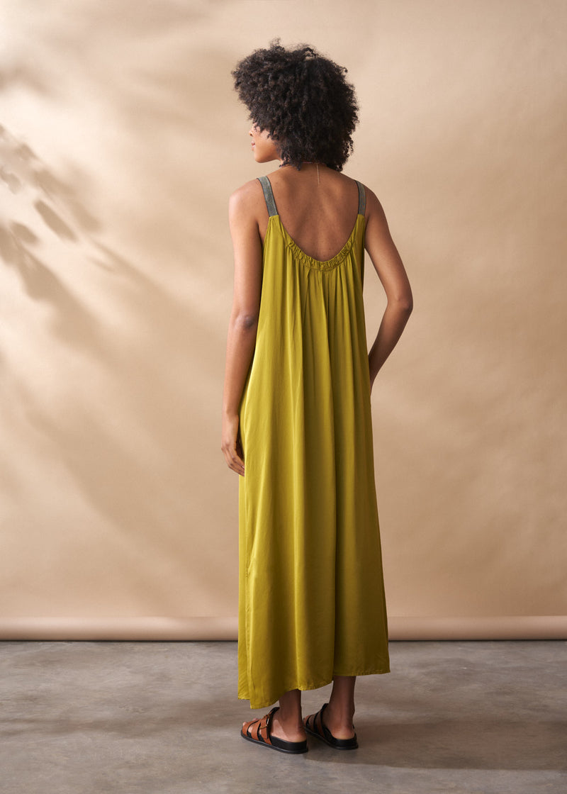 Woman wearing a yellow satin maxi dress standing against a beige wall.