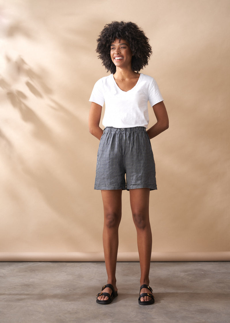 Woman wearing a white t-shirt and checkered shorts against a beige background
