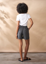 Person wearing a white t-shirt and checkered shorts against a beige background