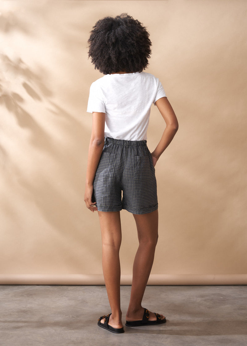 Person wearing a white t-shirt and checkered shorts against a beige background