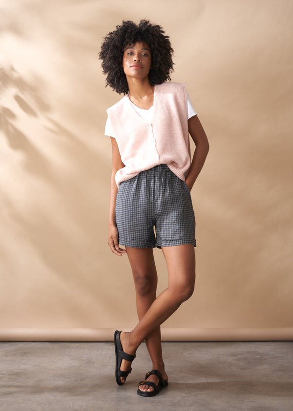 Woman wearing a light pink top and checkered shorts against a beige background