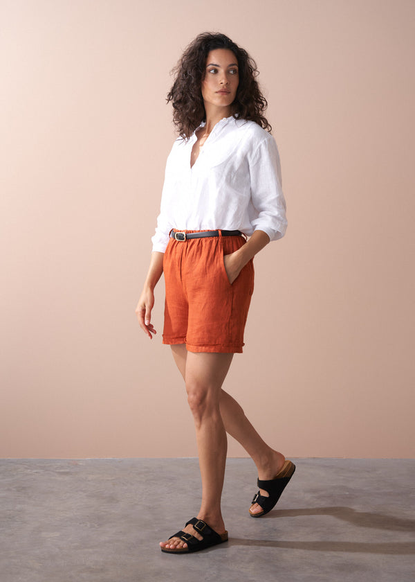 Woman wearing a white shirt and orange shorts against a beige background