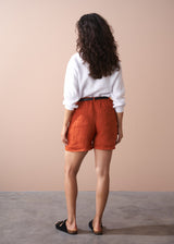 Person wearing orange shorts and a white shirt against a beige background