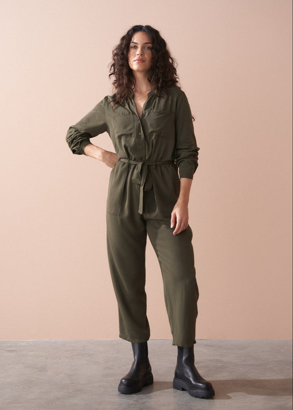 Woman wearing an olive green jumpsuit against a beige background