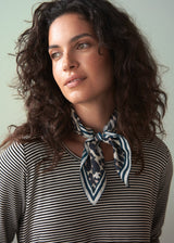 Woman wearing a striped shirt and a patterned scarf against a plain background