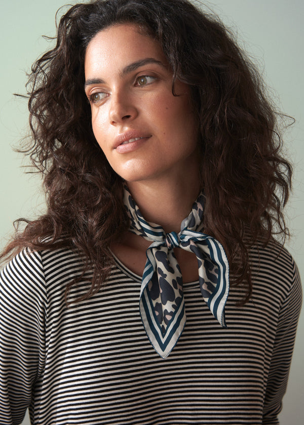 Woman wearing a striped shirt and a patterned scarf against a plain background