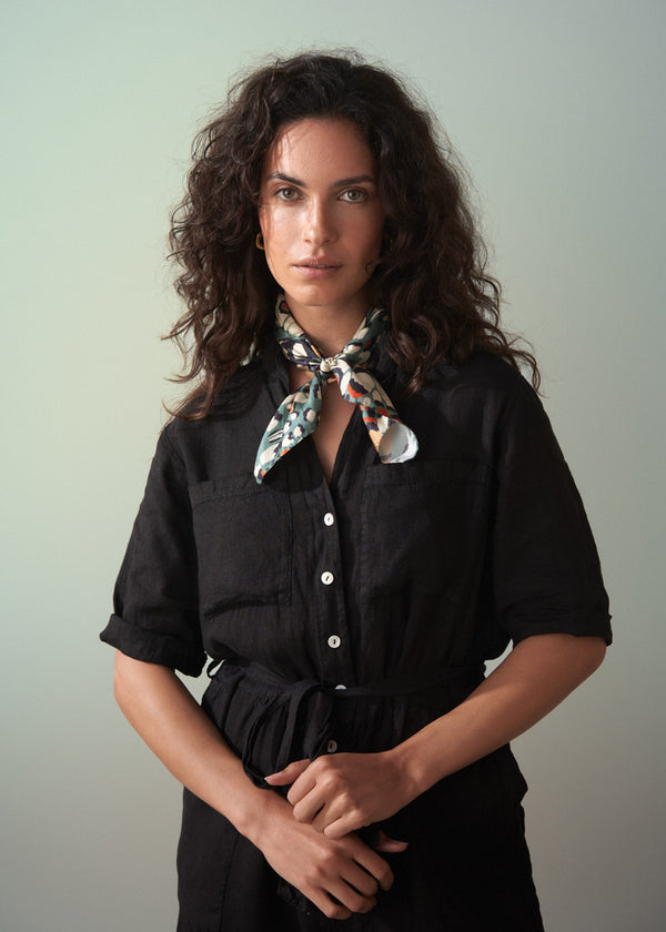Woman wearing a black shirt with a colorful scarf around her neck against a plain background