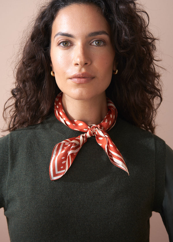 Woman wearing a red patterned scarf around her neck against a beige background