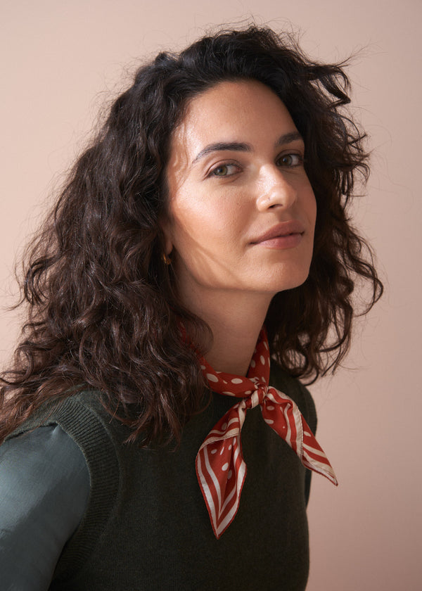 Woman with curly hair wearing a red patterned scarf against a beige background