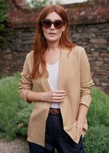 Woman wearing a beige blazer, white vest top and blue jeans in a garden