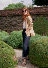Woman wearing a beige blazer, white vest top and blue jeans in a garden