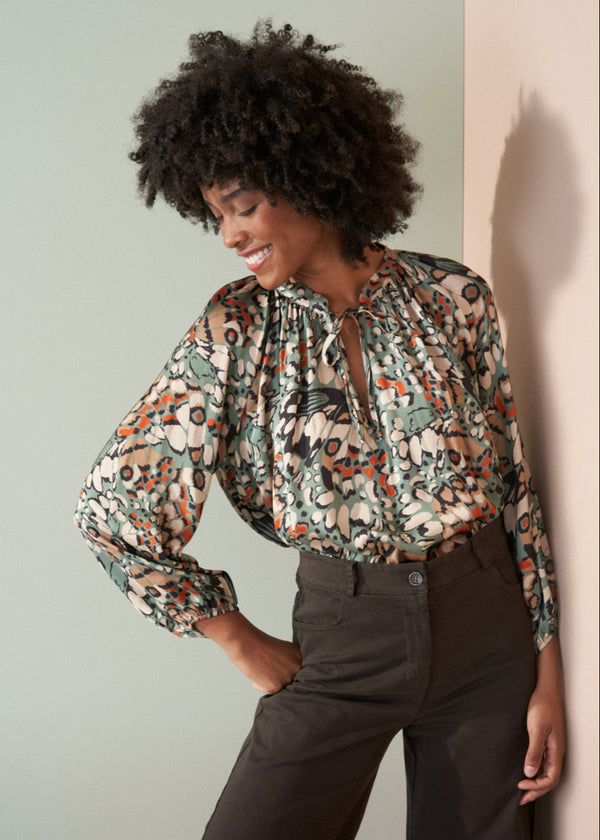 Woman wearing a floral blouse and dark pants against a light background