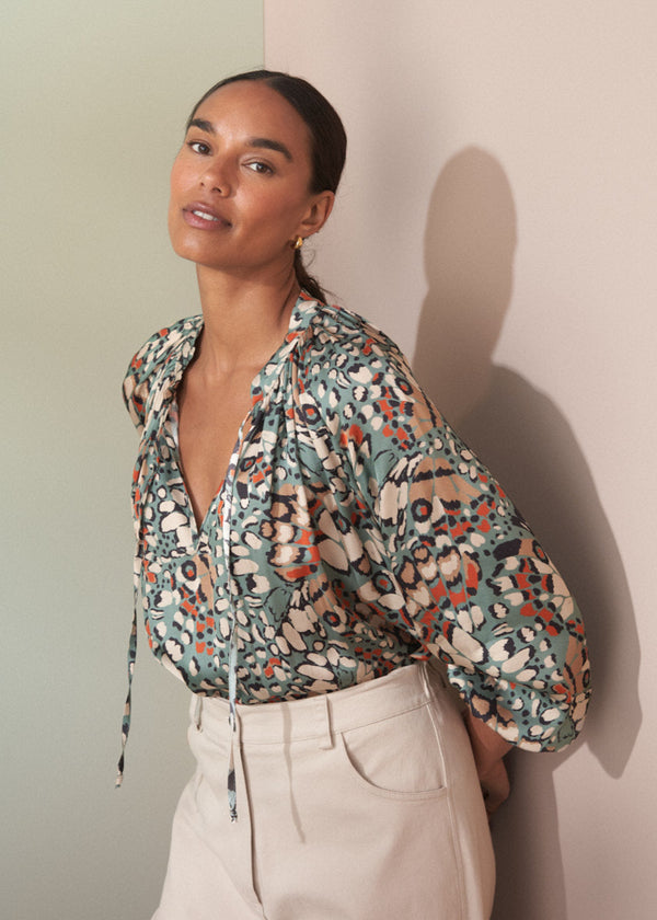 Woman wearing a floral blouse and white trousers against a neutral background