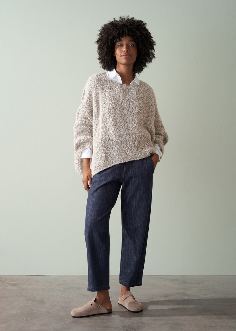 Person wearing an off white boucle sweater and dark blue jeans against a plain background