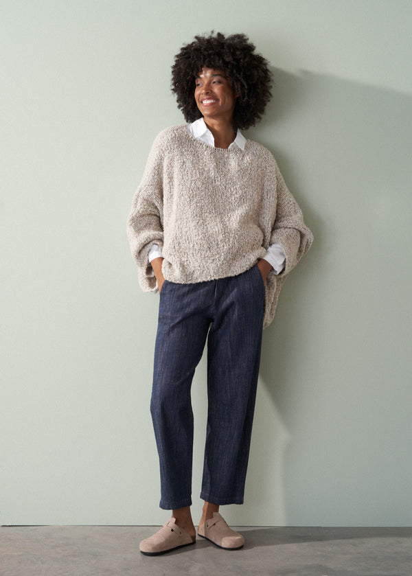 Person wearing an off white boucle sweater and dark blue jeans against a plain background