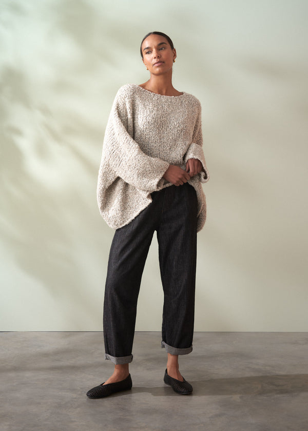 Person wearing a beige sweater and black pants against a plain background
