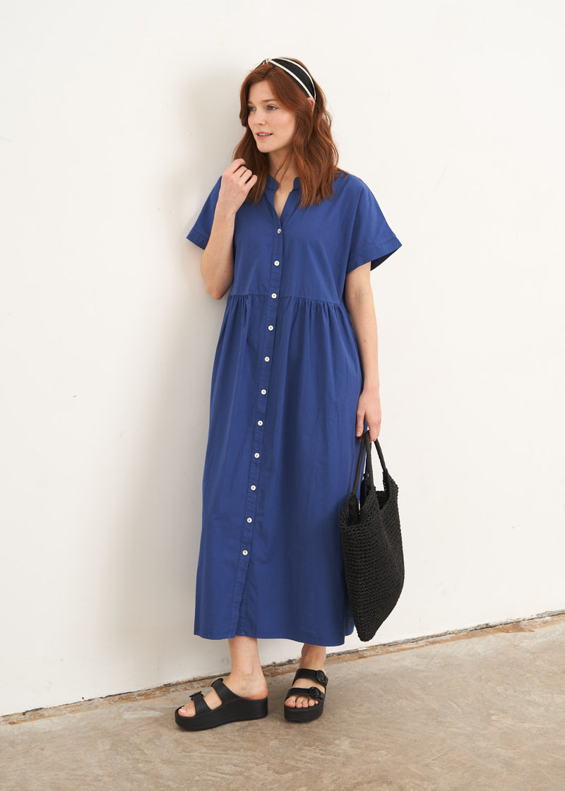 A model wearing a blue relaxed fit button down shirt dress with short sleeves