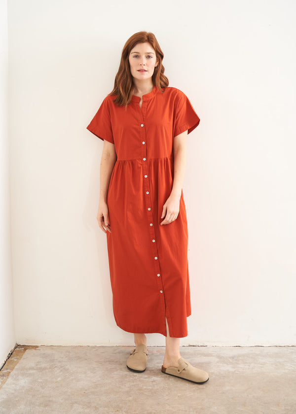 A model wearing a oversized shirt dress in a rusty red tone with mother of pearl buttons